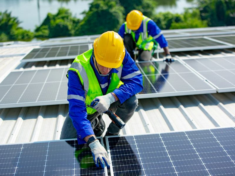 Solar panel installer installing solar panels on roof of warehouse Solar panel installer installing solar panels on roof of warehouse